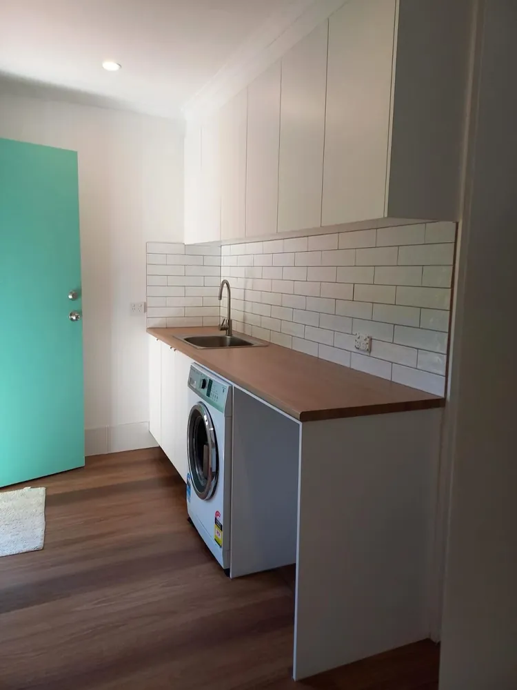 Renovated laundry with timber benchtop, undermount sink, subway tile splashback and overhead cabinetry