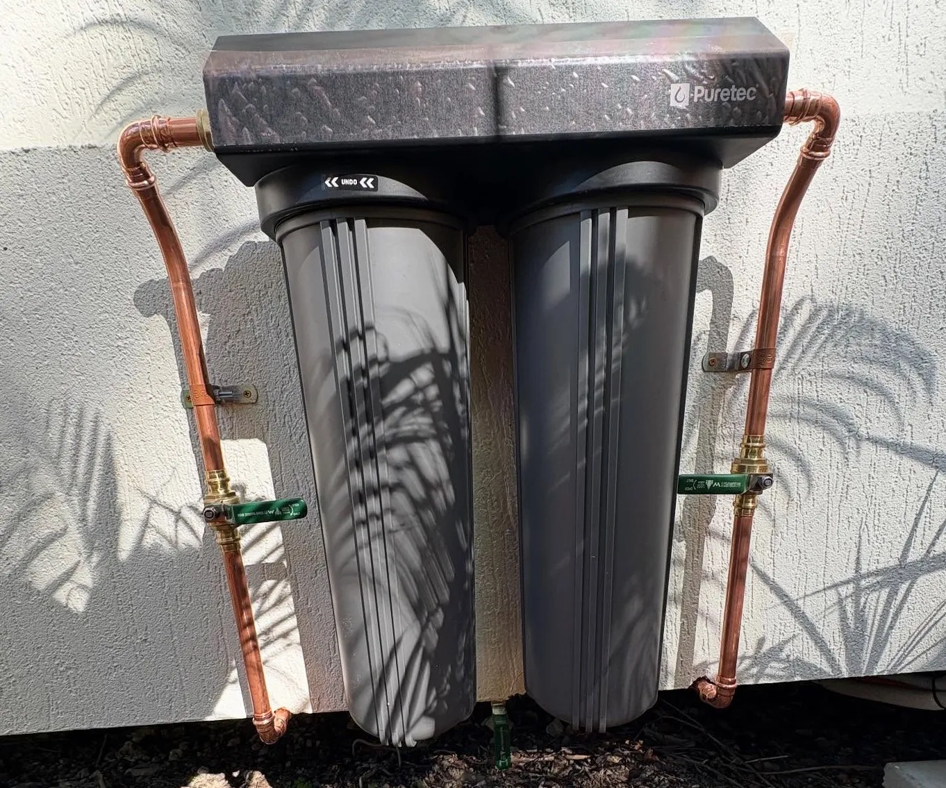 Puretec twin whole house water filter installed on an exterior wall with copper pipework and isolation valves