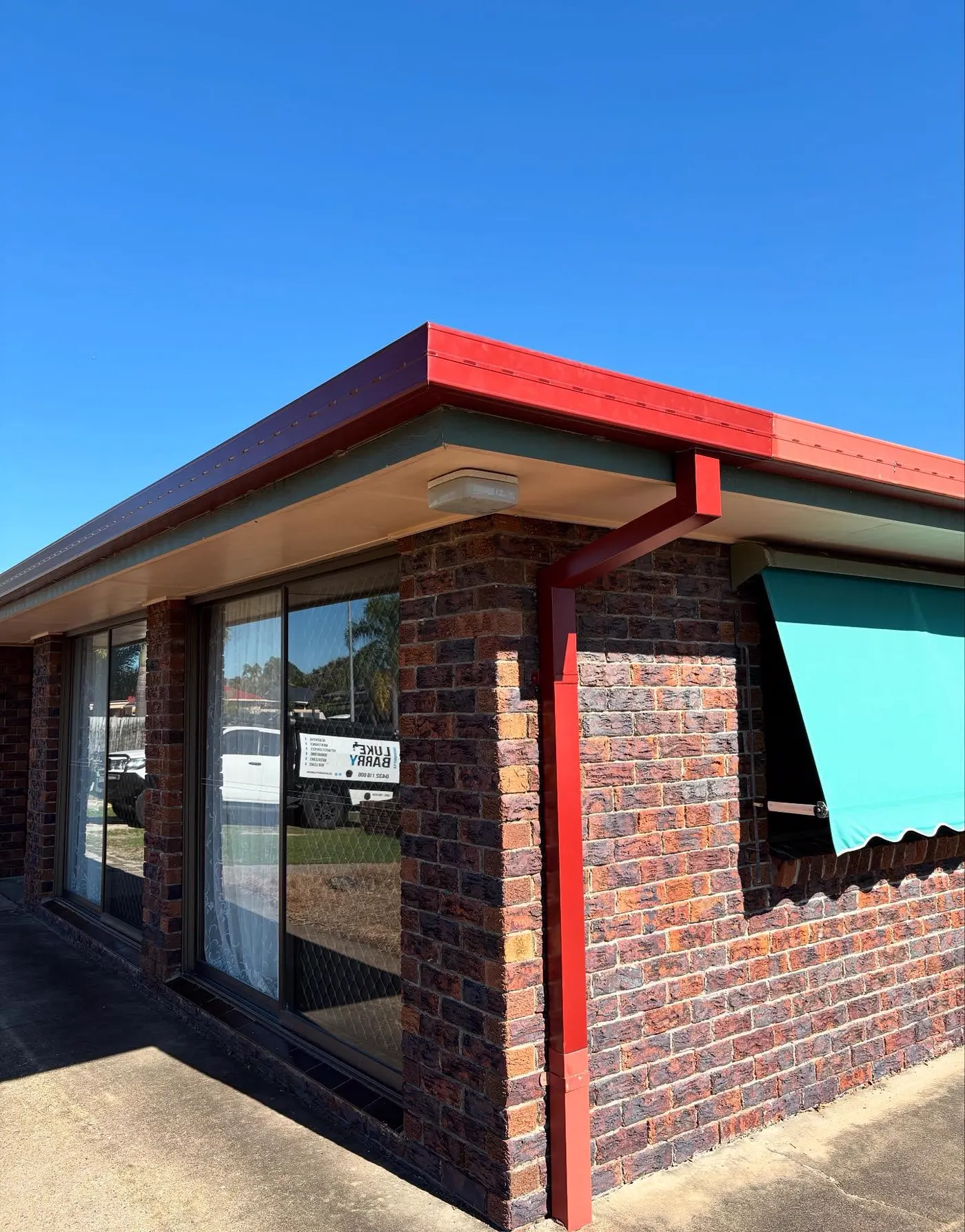 New red Colorbond gutter, fascia and downpipe installed on a brick home on the Gold Coast
