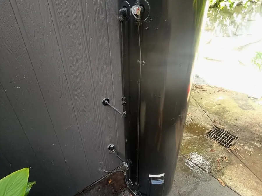 Old black Vulcan hot water system leaking onto concrete in a narrow courtyard