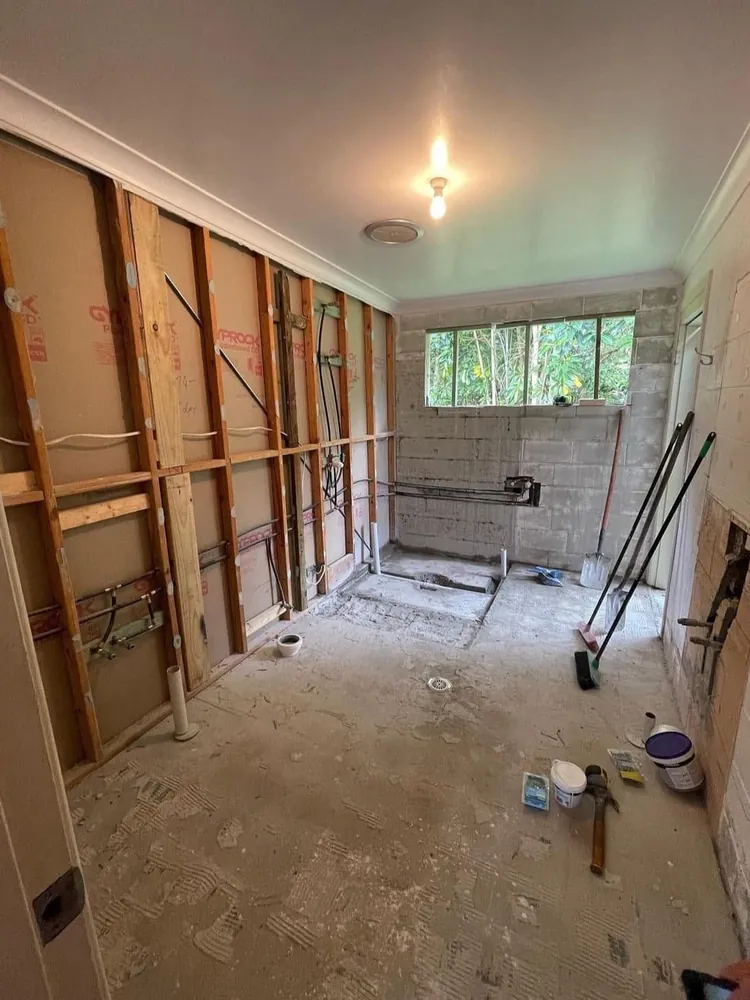 Stripped-back bathroom during renovation with exposed wall framing and rough-in plumbing
